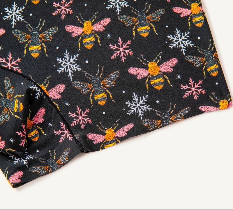 PureSnug biker shorts fabric with vibrant bees & snowflakes on black, blending nature and winter motifs.