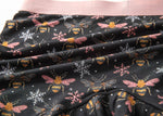 Close-up of fabric with a pattern of bees with pink wings and pink and white snowflakes on a black background.