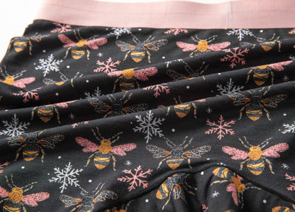 Close-up of fabric with a pattern of bees with pink wings and pink and white snowflakes on a black background.
