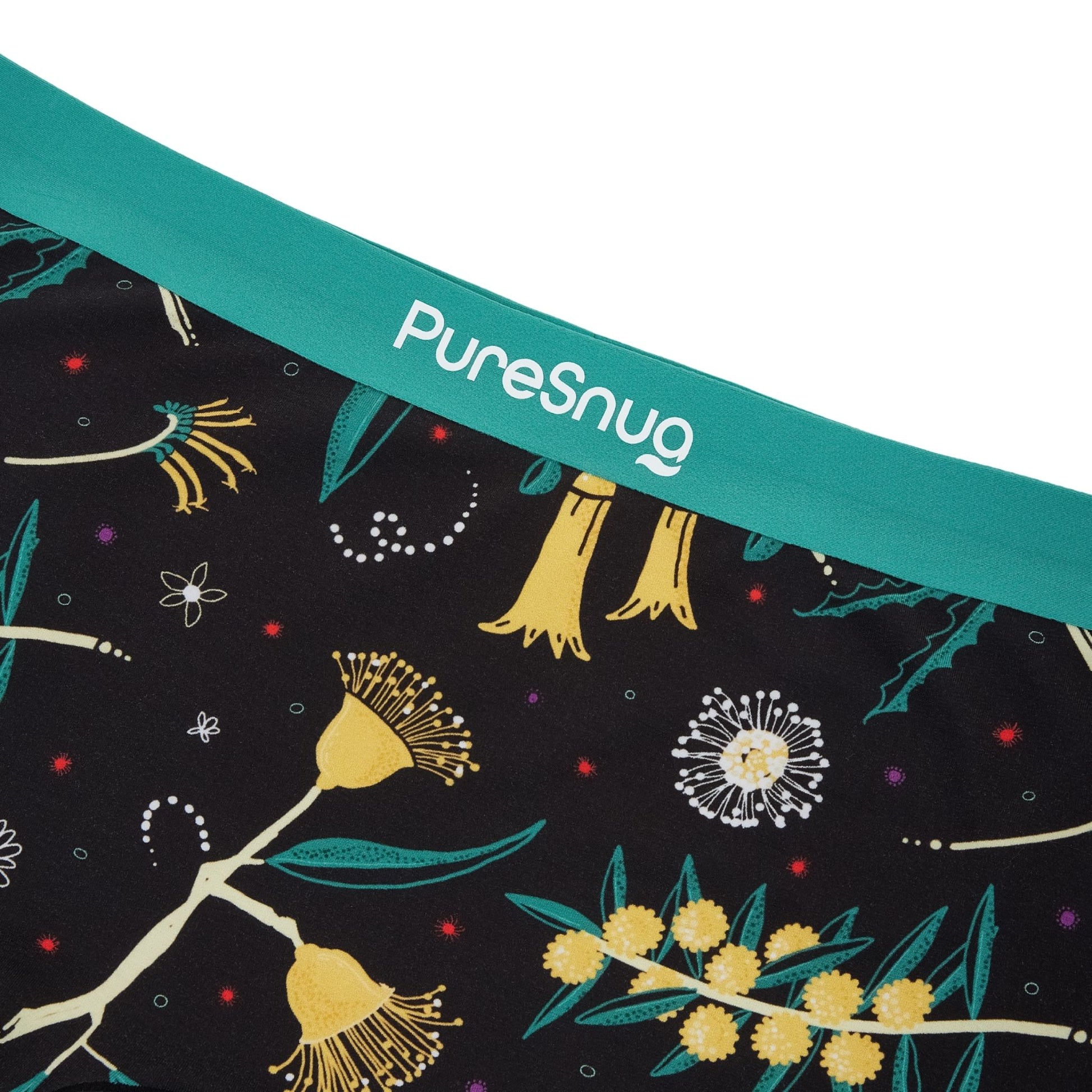 Close-up of a fabric edge with vibrant botanical prints on a black base, finished with a teal waistband