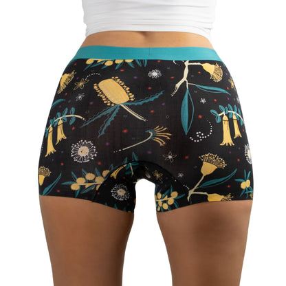 Close-up of the back view of a woman wearing PureSnug Golden Snug floral boyshorts/boyleg with a black background