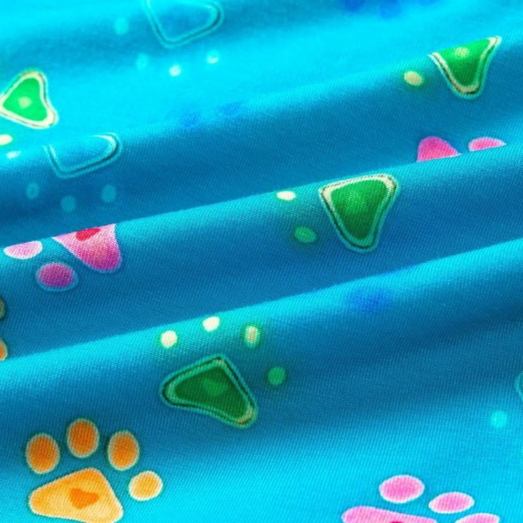 Close-up of vibrant blue fabric featuring colorful paw prints and geometric shapes in pink, green, and orange patterns.