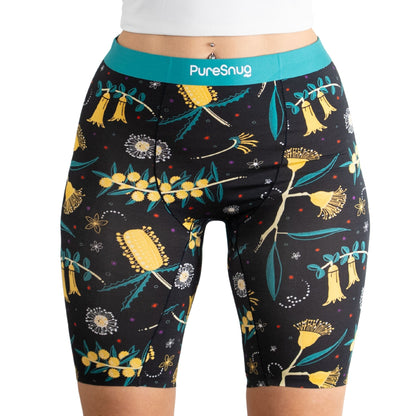 A model wearing black patterned biker shorts featuring colorful floral designs and a turquoise PureSnug waistband.