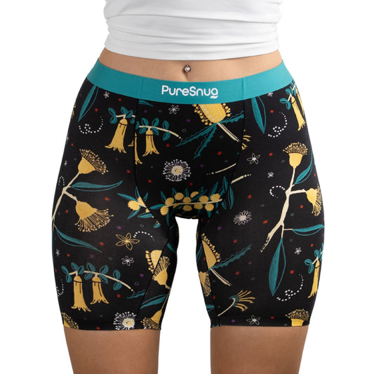 A close-up of a person wearing PureSnug Golden Snug boxer brief in floral-patterned black shorts with a turquoise waistband