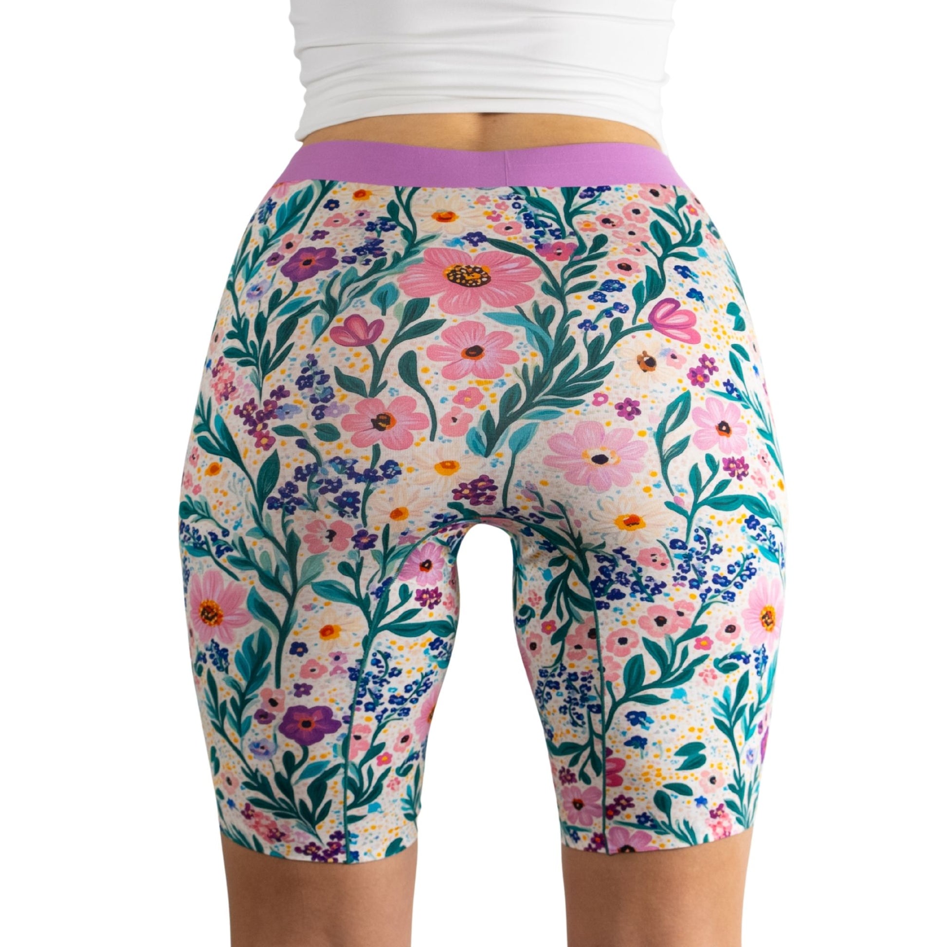A model in a white top showcases colorful, floral-patterned bike shorts, highlighting vibrant blooms and greenery.