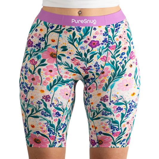 A model wearing colorful floral print biker shorts with a purple waistband, paired with a white cropped top.