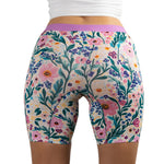 Woman wearing PureSnug boxer briefs with vibrant floral pattern in pink, purple, and yellow, conveying a cheerful mood.