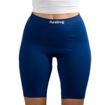 A model wearing navy blue PureSnug high-waisted bike shorts, paired with a white cropped top
