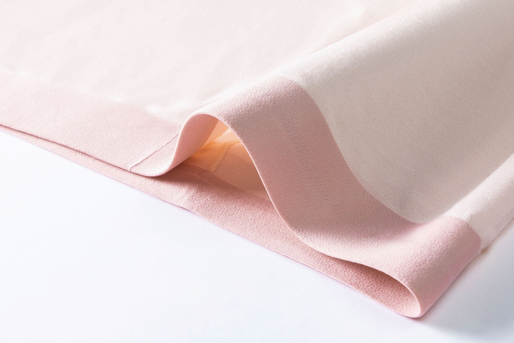 Close-up of a neatly folded, soft pink and cream fabric with a smooth texture. It conveys a sense of elegance and calm.
